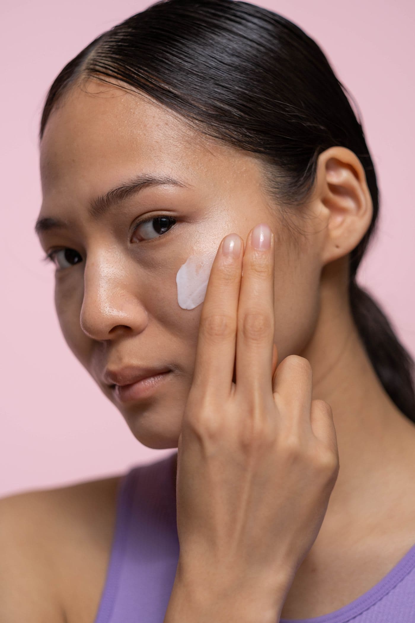 A person applying cream to their cheek with two fingers