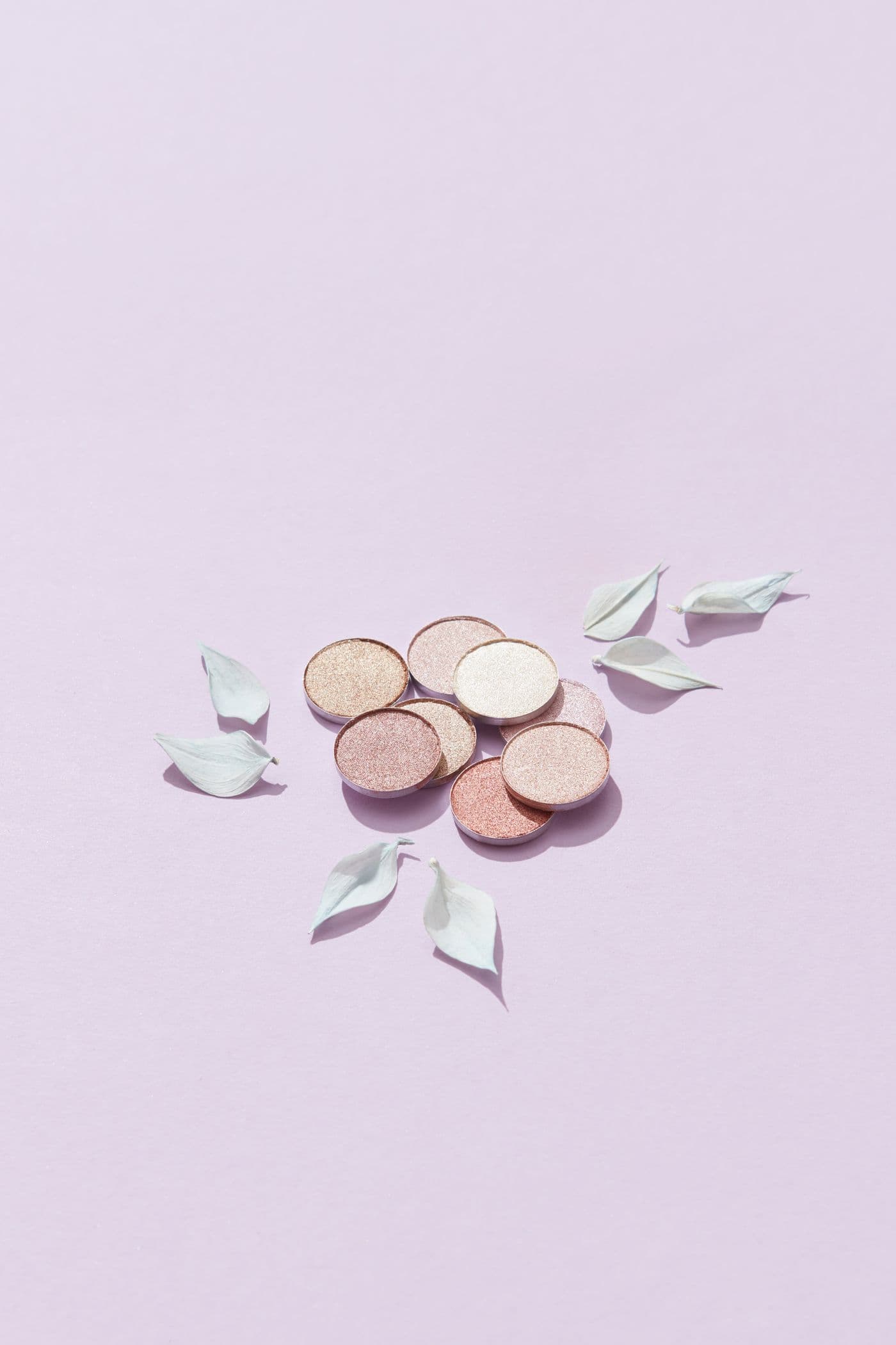 Copper-toned cosmetic pans arranged on a soft lilac background