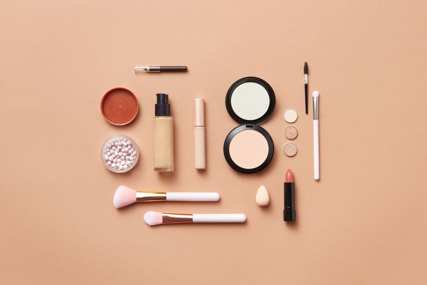 A flatlay of skincare and cosmetics on a warm neutral background