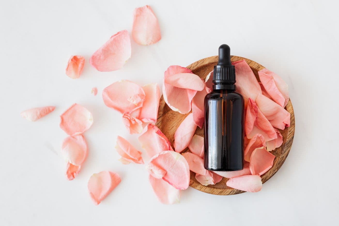 An amber dropper bottle resting on a bed of pink rose petals